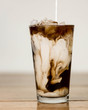 Iced coffee on a wood table with cream being poured into it showing the refreshing drink with a clean background
