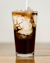 Iced Coffee On A Wood Table With Cream Being Poured Into It Showing The Refreshing Drink With A Clean Background