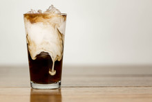 Iced Coffee On A Wood Table With Cream Being Poured Into It Showing The Refreshing Drink With A Clean Background