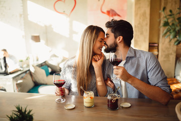 Wall Mural - Happy couple drinking red wine at fashion restaurant. Handsome man kissing his girlfriend in nose.