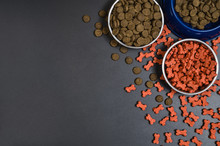 Dry Dog Pet Food In Bowl On Blach Chalkboard Background Top View. Pet Feeding Concept Backgrounds With Copy Space. Photograph Taken From Above.