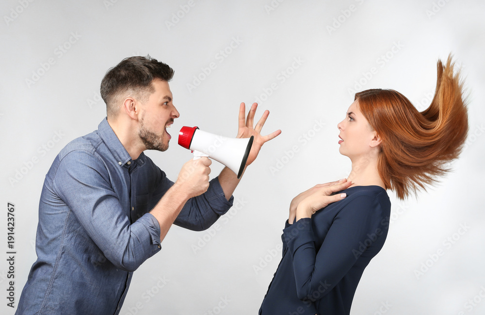 Angry man with megaphone scolding his wife on light background