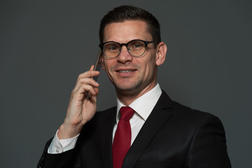 Wall Mural - Successful young businessman in formal suit talking to someone on smartphone discussing good deal on gray background