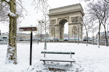 Winter in Paris in the snow. The Arc de Triomphe with a public bench covered in snow in the foreground.