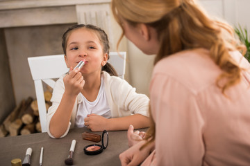 Wall Mural - selective focus of mother and little daughter applying makeup together at home