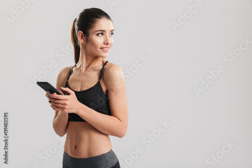 Εκτύπωση καμβά Portrait of well-built smiling woman looking back while holding smartphone in ha