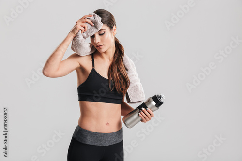 Αφίσα Tired young sportswoman in tracksuit drinking water and wiping sweat with towel