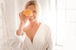 Fresh energy. Happy delighted nice woman holding an orange half and smiling while using it for cosmetic procedures