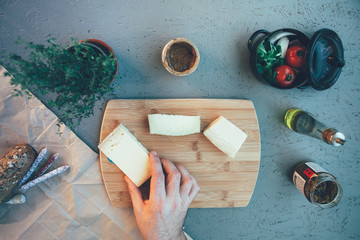 high angle view of and hand picking up cheese from a chopping board and ingredients around the table