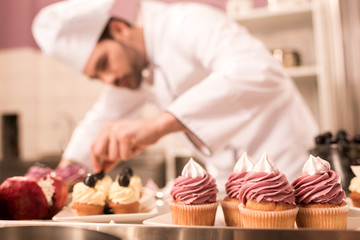 Wall Mural - selective focus of confectioner decorating cupcakes in restaurant kitchen