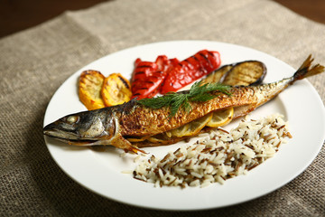 Healthy and proper food, grilled fish and vegetables with lemon and black and white rice on a white plate. Against the background of sacking and a wooden table. Low-calorie food