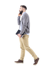 Wall Mural - Relaxed successful businessman on the phone walking and carrying tablet computer. Full body length portrait isolated on white studio background. 