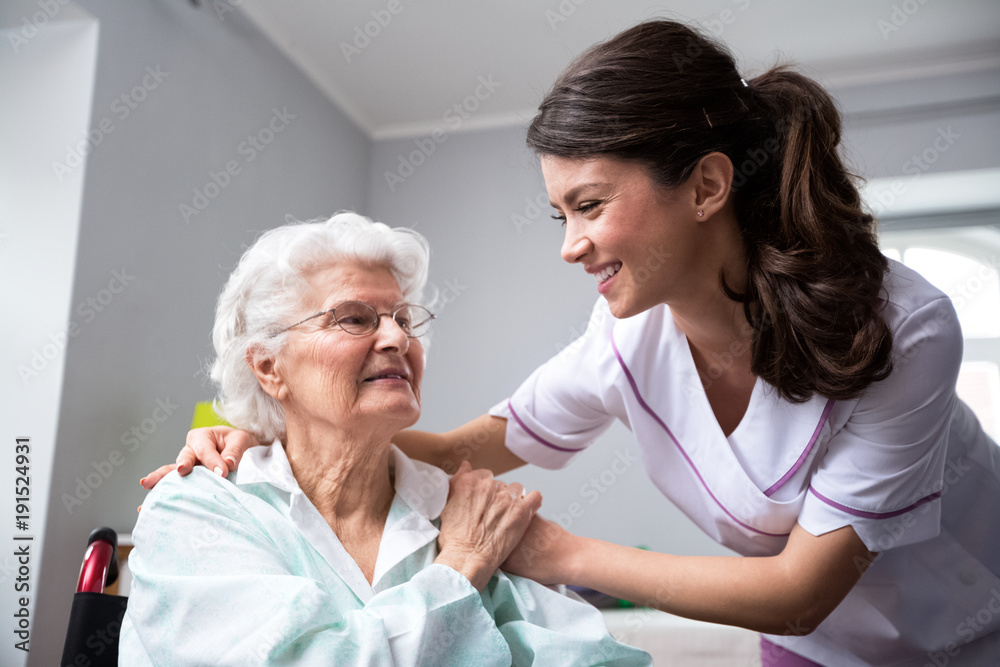 Smiling nurse and old woman patient at wheelchair - obrazy, fototapety, plakaty 