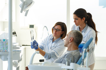 Dentist and her assistant in dental office talking with male patient and preparing for treatment.Examining x-ray image.