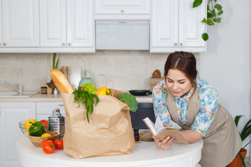 Young housewife with recipes book in the kitchen