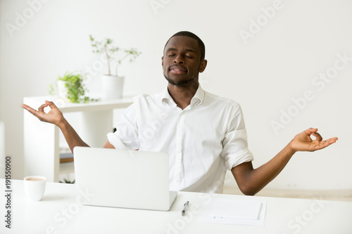Calm Happy African American Man Meditating At Home Office Desk