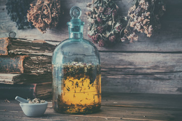 Wall Mural - Tincture or potion bottle, old books, mortar and hanging bunches of dry healthy herbs. Herbal medicine. Retro styled.