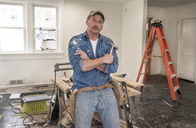 Male Carpenter Wearing Leather Tool Belt And Holding Hammer Leaning Against Saw Horse Work Table With Chop Saw In Home Remodel