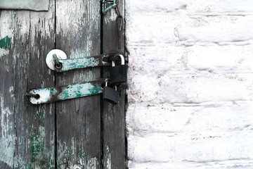 Old wooden doors closed on two padlocks against the backdrop of a painted brick wall of white color. Doors with forged metal elements