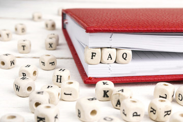 Word FAQ written in wooden blocks in notebook on white wooden table.