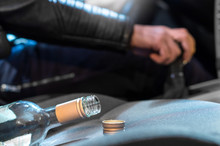 Drunk Driving Concept. Young Man Driving Car Under The Influence Of Alcohol. Hand On Gear Stick. Close Up Of Empty Bottle Of Wine On Front Seat. Traffic Safety Risk.