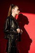 © LIGHTFIELD STUDIOS - side view of stylish girl with ponytail hairstyle posing in black leather jacket for fashion shoot on red