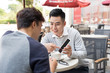 © makistock - Asian young men enjoying watching on mobile phone together in cafe with coffee on the table.