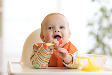 Wall Mural - happy baby boy waiting for food with spoon at table