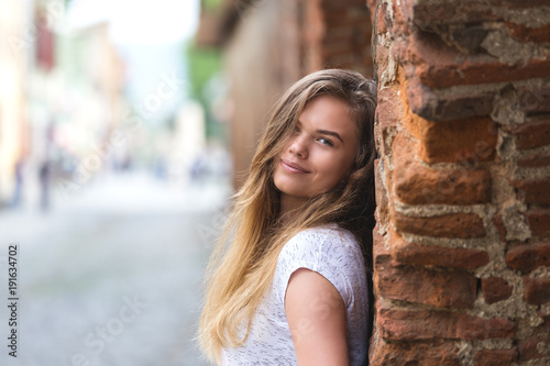 Fotografía Young beautiful girl posing on city street against backdrop of vintage wall, smi