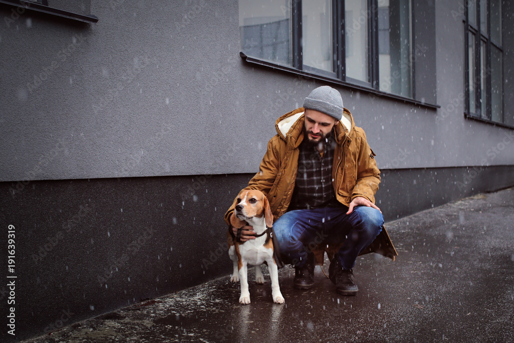 Handsome young hipster walking his dog outdoors on snowy day