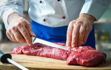 Wall Mural - Hands of male chef in uniform cutting big piece of beef