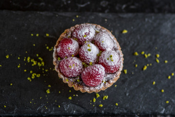Wall Mural - raspberry tart cake on black slate plate with pistacio crumbs and powder sugar