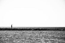 Lonely Child Walks On A Thin Coastline. Minimalistic Black And White Photo.