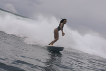 Side View Of Woman In Wetsuit Surfing On Sea Against Cloudy Sky