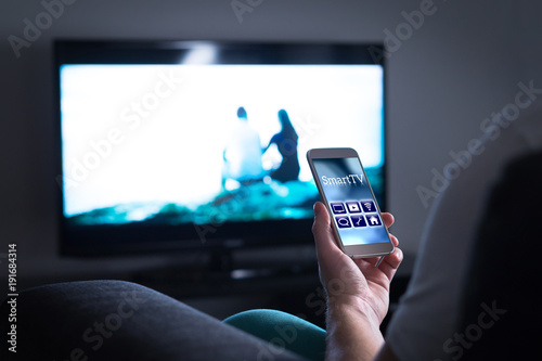 Fotografía Man watching television and using smart tv remote control application on mobile phone