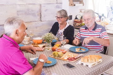 Group of senior people having lunch together at home. She smiles and other eat serious. Salami bread and vegetables on the table