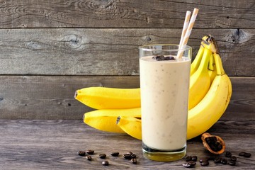 Wall Mural - coffee, banana smoothie in a tall glass with coffee beans and bananas in background. side view, agai