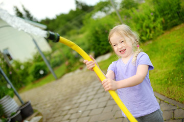 Poster - Adorable little girl playing with a garden hose on warm summer day