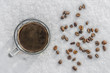 hot mug of black coffee in cold snow, coffee beans scattered