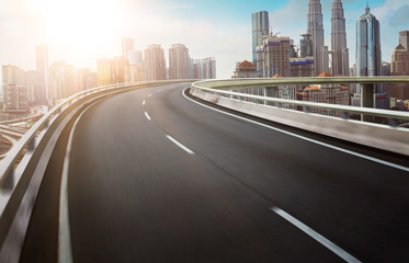 Wall Mural - Motion curvy flyover asphalt highway road with modern cityscape skyline view  . Sunrise scene .