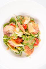 Baby spinach, dry sausage, matured cheese, roast tomatoes, thyme-balsamic vinaigrette salad on a white background