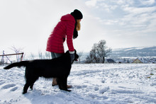 Woman On A Walk With Her Black Dog, Training A Dog Command Stay In A Winter Landscape, Bright Sky 