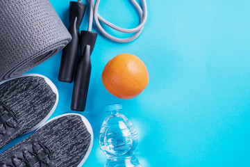 The concept of healthy lifestyle. Sport shoes, bottle of water, apple and yoga mat with copy space on blue background. Exercise equipment. Sport life, top view, flat lay.