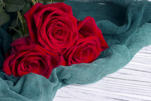 Three Red Roses On Green Textile On White Wooden Background.