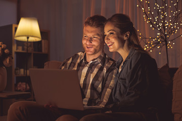 Poster - Portrait of happy woman and outgoing bearded man looking at laptop while sitting on sofa. Entertainment concept