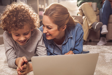 Poster - Happy kid and beaming mother watching at notebook computer while locating on carpet. Appliance concept