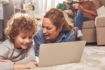 Poster - Portrait of beaming mom and outgoing boy watching at appliance while locating on carpet. Technology concept