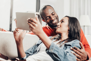 Man and woman in love relaxing on comfortable sofa with tablet. They are looking at each other with eyes of love and smiling