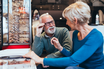 Poster - Happy senior couple choosing together eyeglasses frame in optical store. 