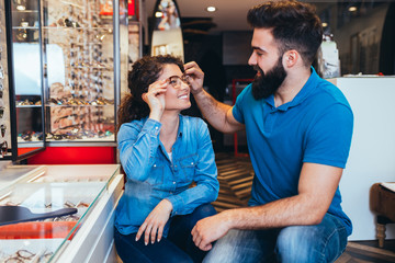 Wall Mural - Happy young couple choosing together eyeglasses frame in optical store. 